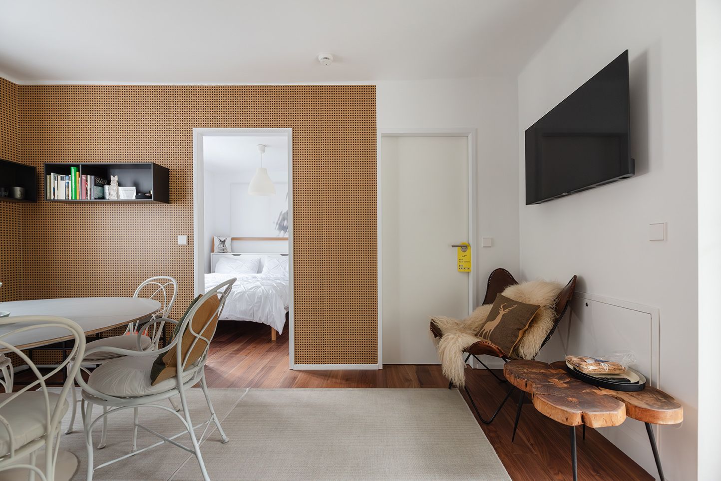 Interior view of a modern furnished room with wooden wall, dining table, chairs and a TV on the wall.