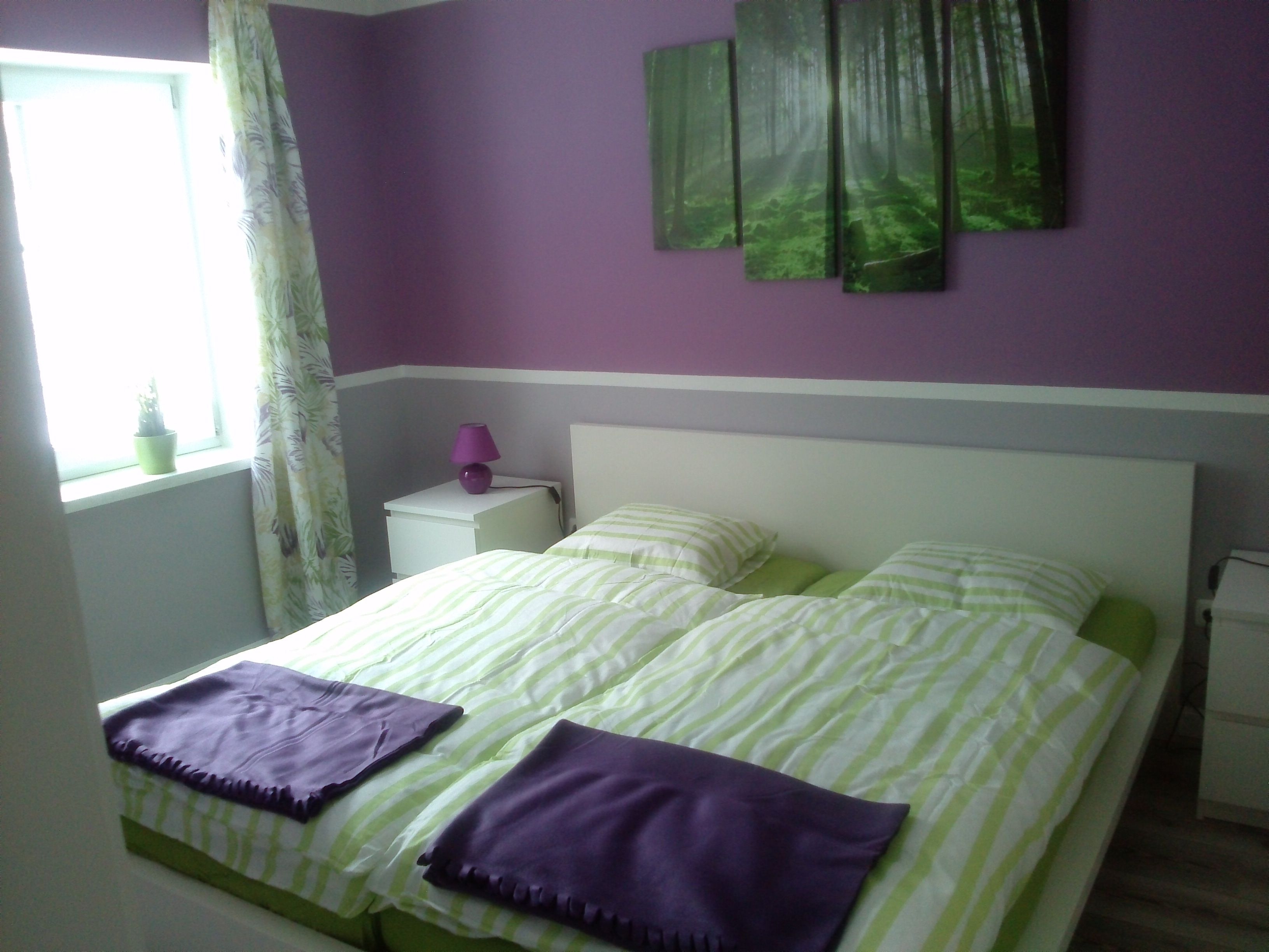 Bedroom with purple and green decoration, double bed, bedside table and window.
