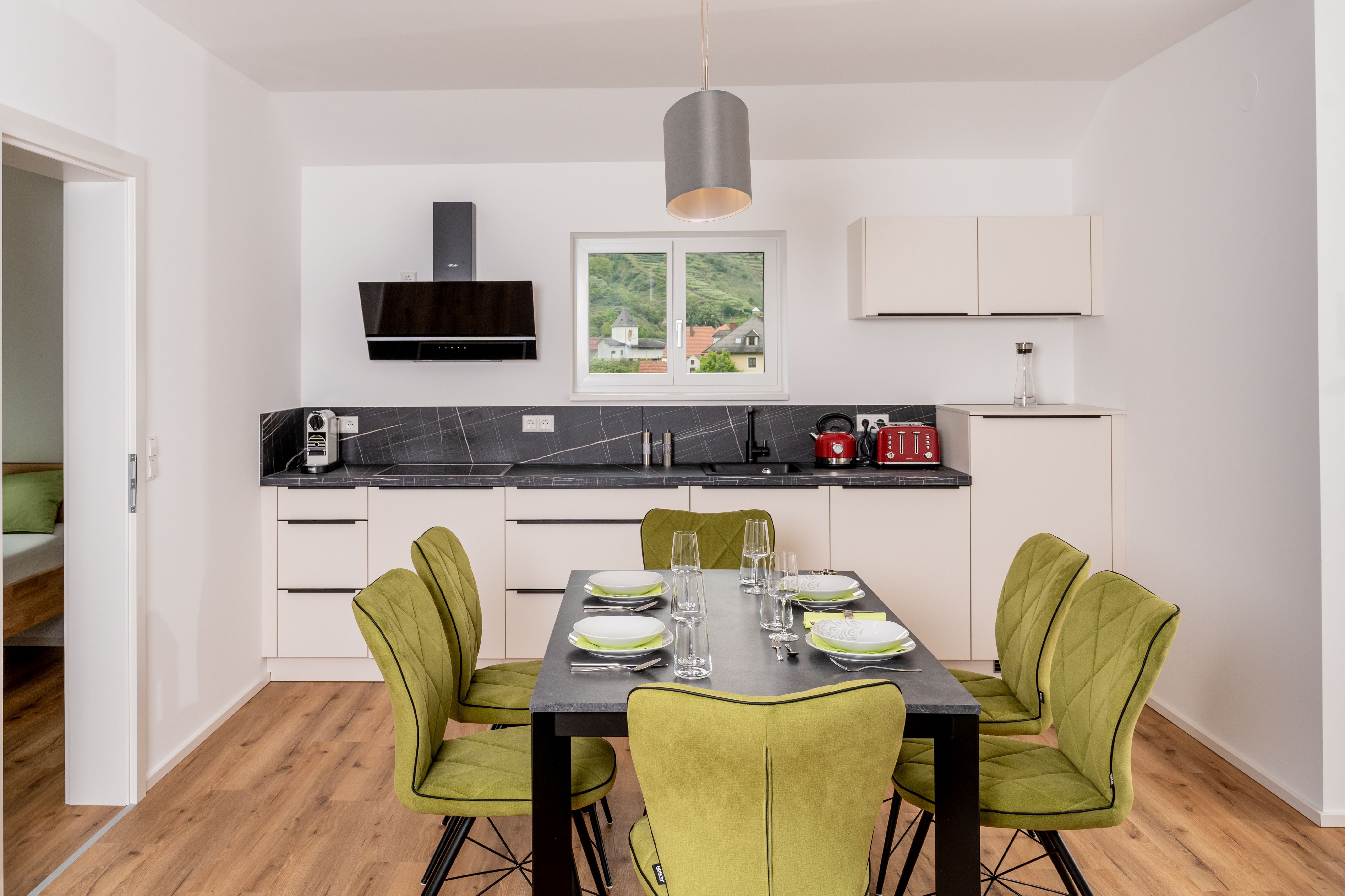 Modern kitchen with dining table and green chairs, window with view of the hills.