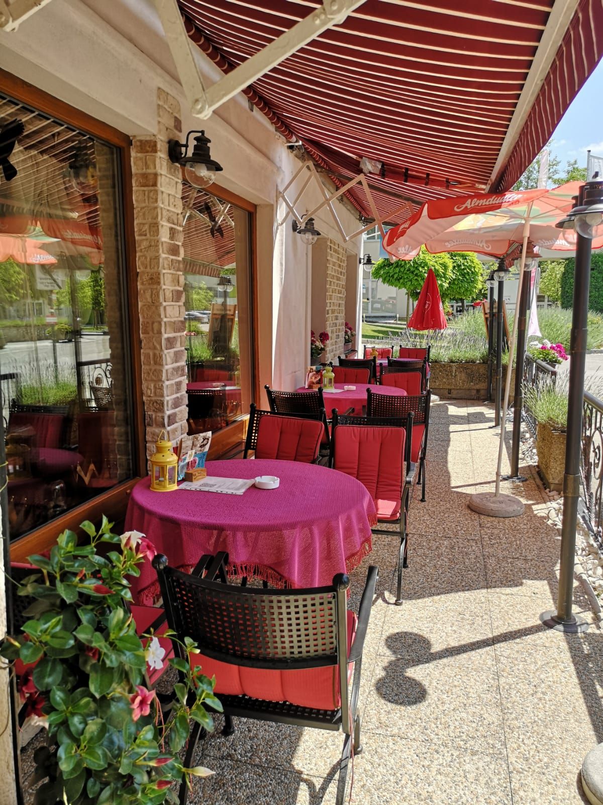 Outdoor terrace of a café with red tables and chairs under a striped awning.