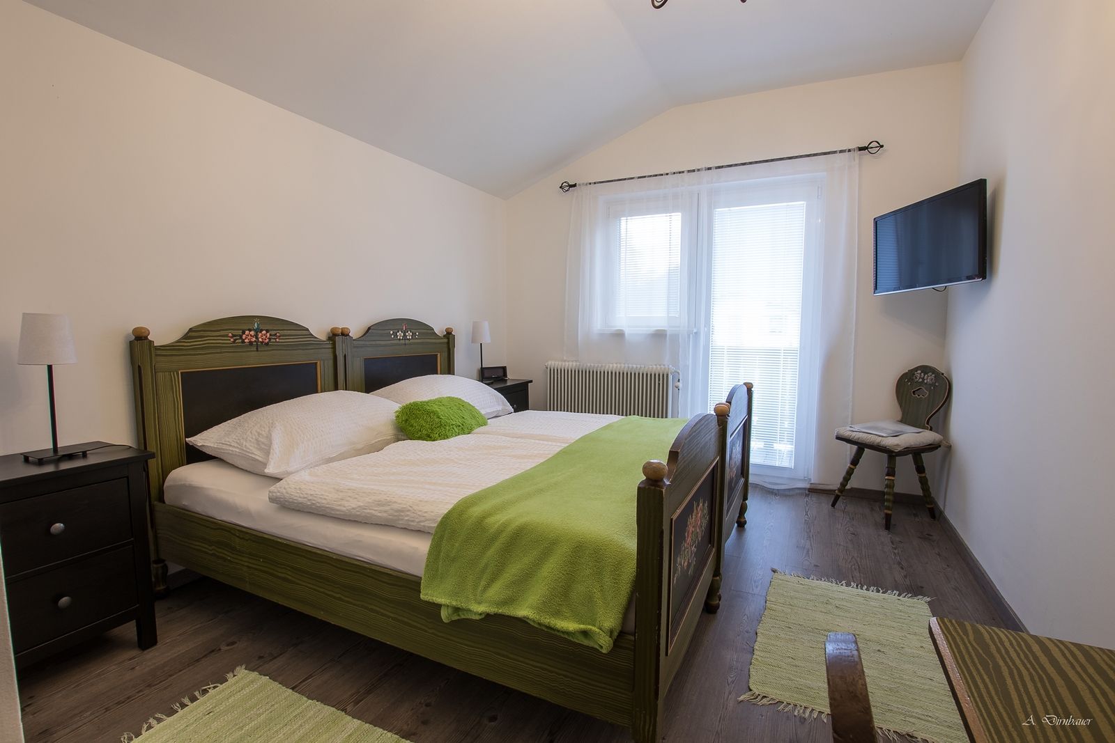 Cozy bedroom with double bed, green comforter and TV on the wall.