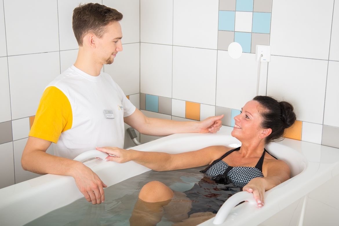 A woman in a sulphur bath is cared for by a therapist.