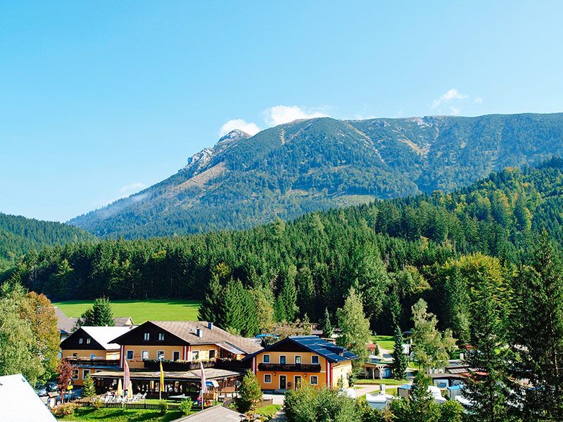 View of a camping site with buildings in front of a wooded mountain massif.