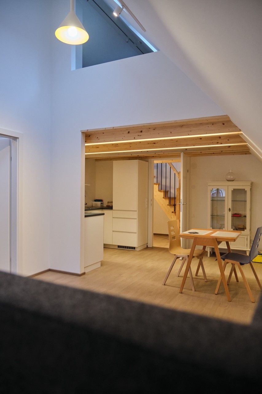 Interior view of a modern living room with wooden staircase, dining table and kitchen area.