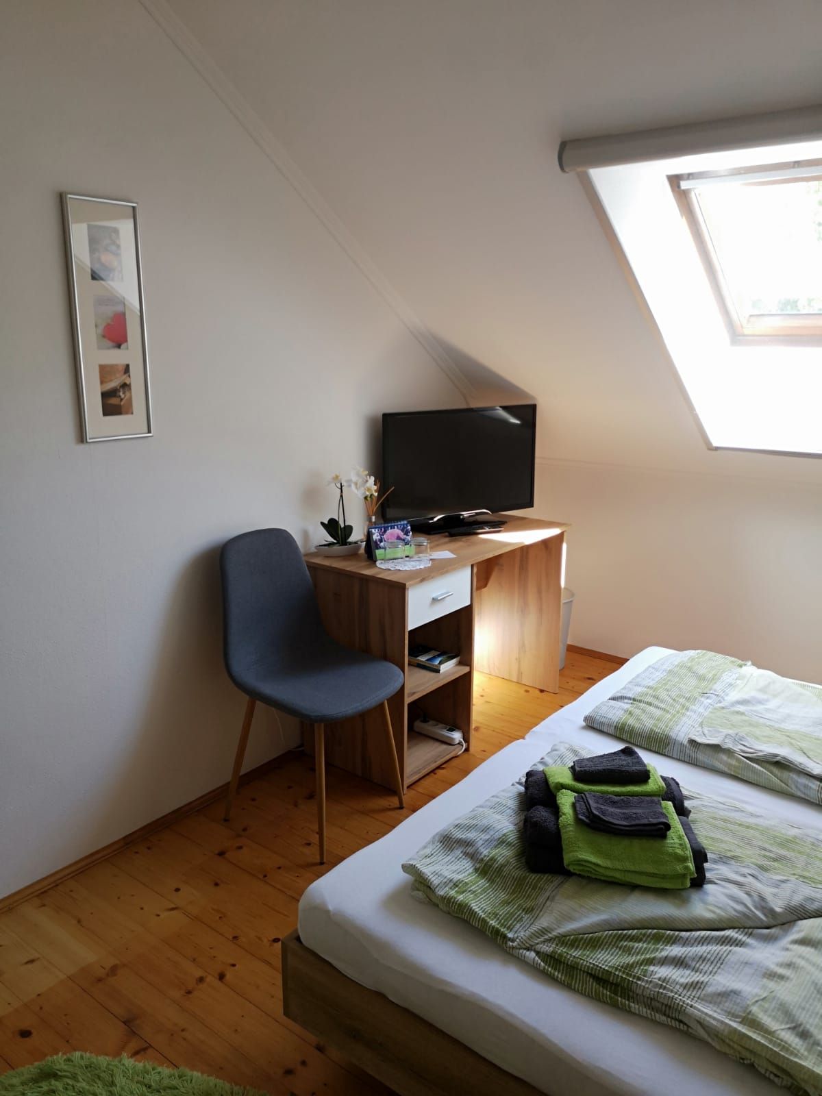A cozy room with a bed, a small desk with TV, a chair and a skylight.
