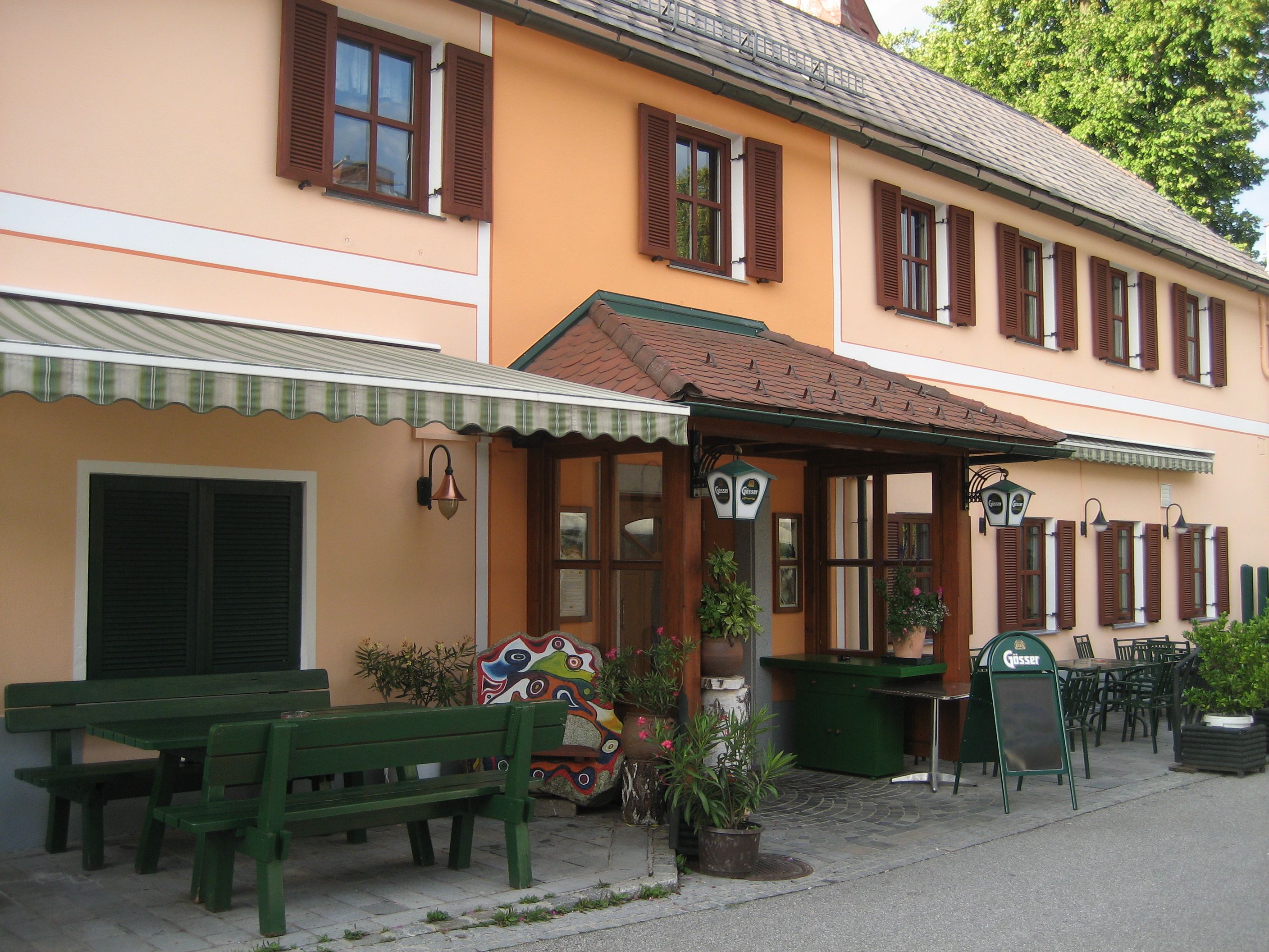 Entrance to a traditional inn with an orange façade and green wooden furniture outside.
