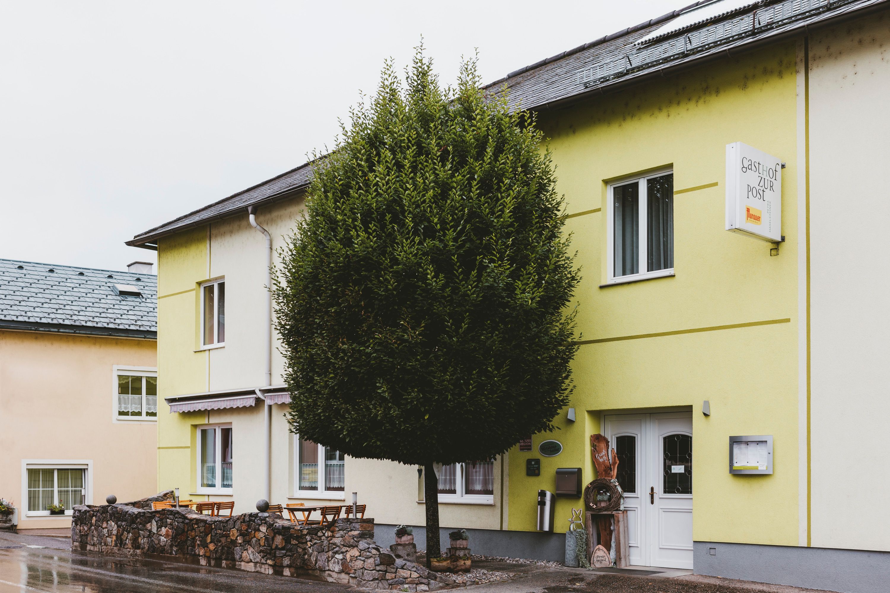 Exterior view of an inn with a yellow façade and a tree in front of it.