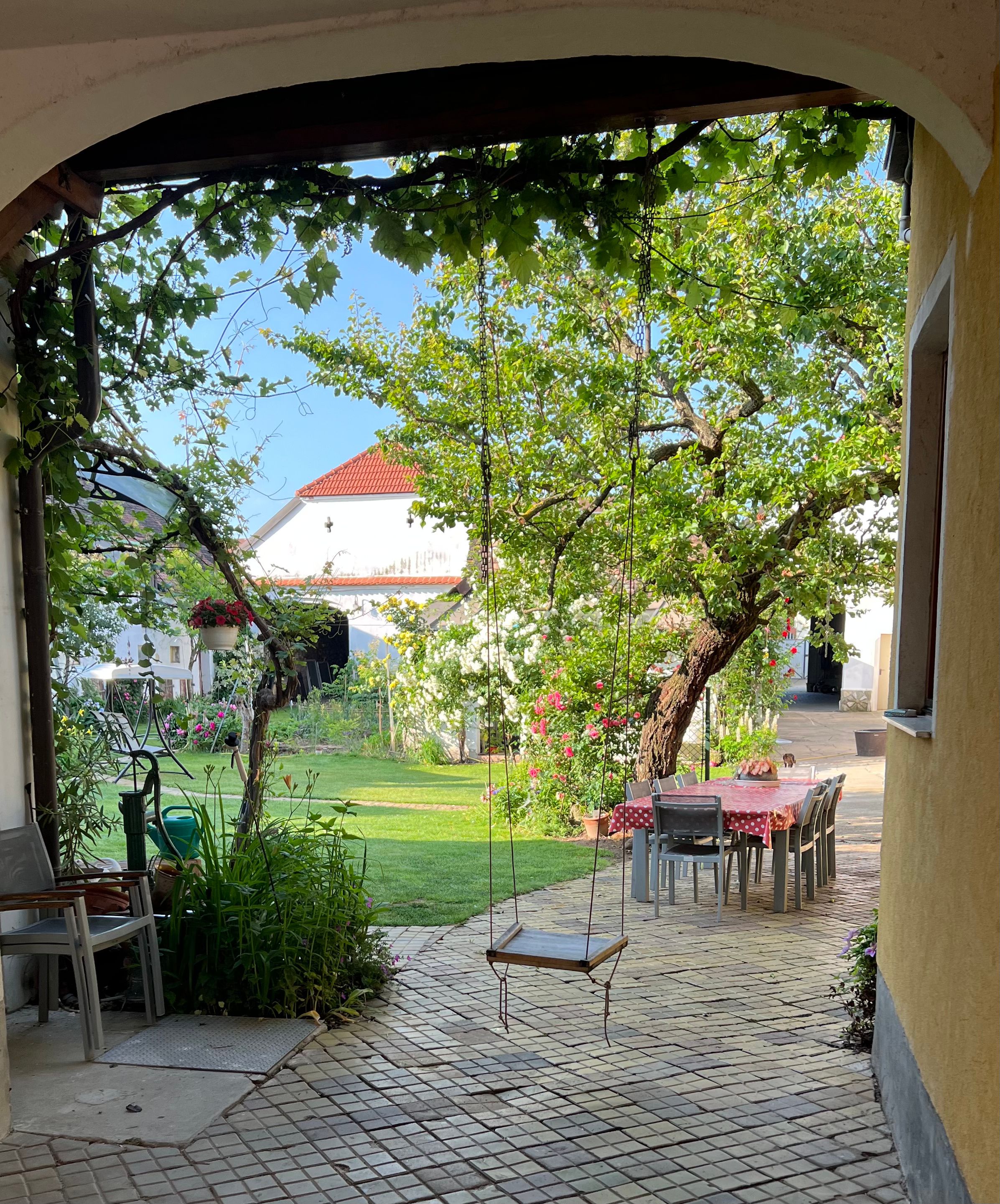 An idyllic garden with a swing, a table with chairs and flowering plants.