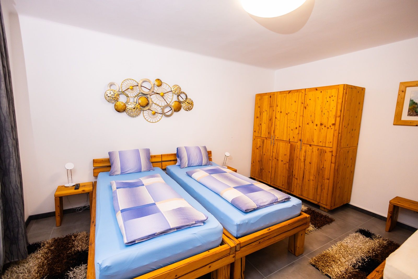A cozy bedroom with two single beds, blue bed linen, wooden furniture and decorative wall art.