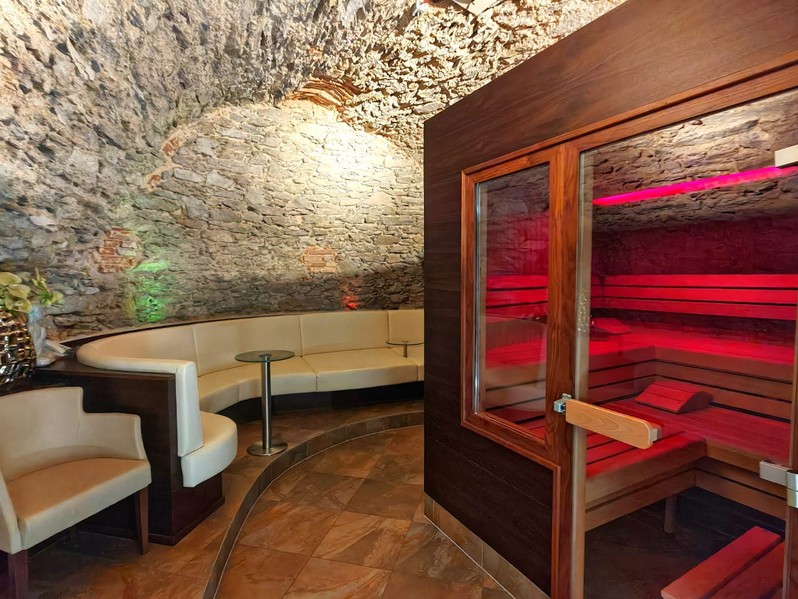 A cozy wellness area with a sauna and a seating area in a room featuring a vaulted stone wall.