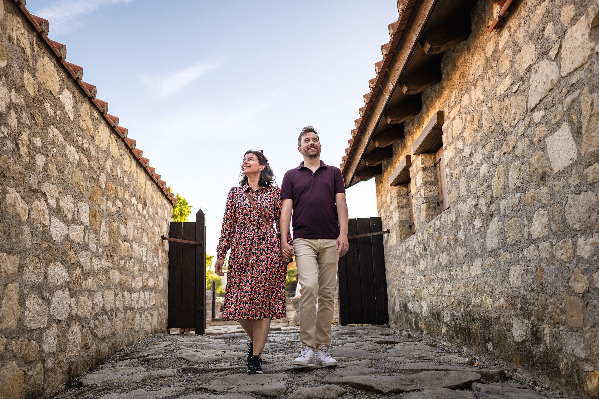 Couple walking through the Roman quarter of the Roman city of Carnuntum. Stone houses to the left and right. 