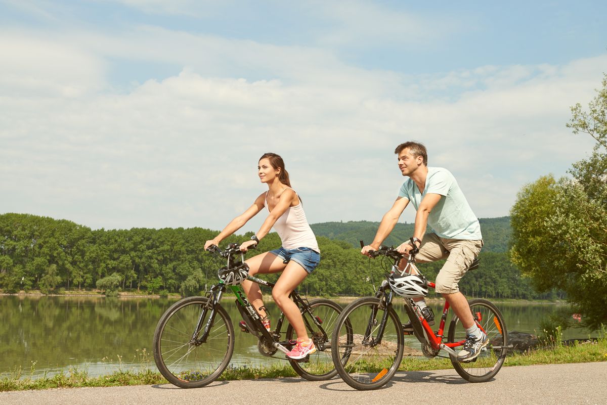 Two people riding bicycles along a river in sunny weather.