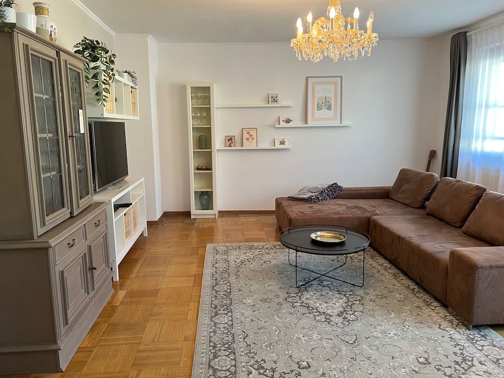 Living room with brown sofa, carpet, chandelier and TV cabinet.