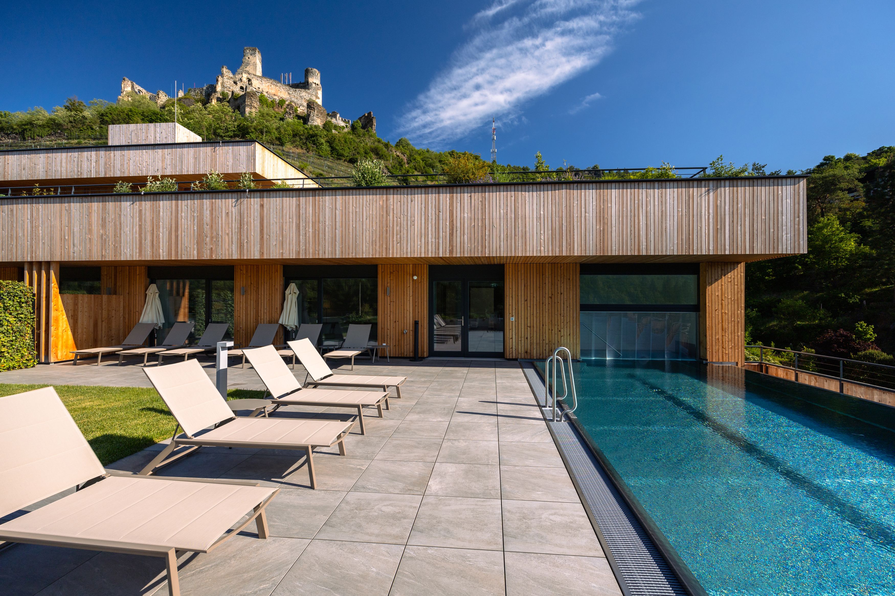 Modern hotel with pool and sun loungers, castle in the background.