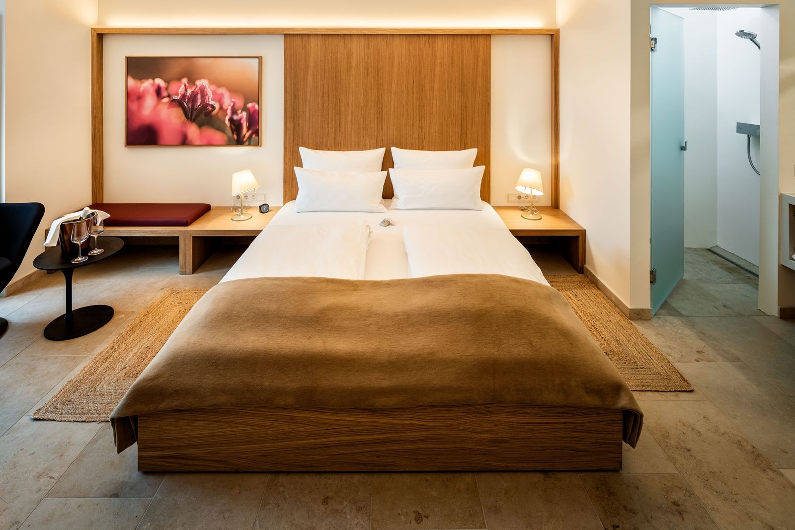 Modernly furnished hotel room with double bed, bedside tables, lamps and a picture on the wall.