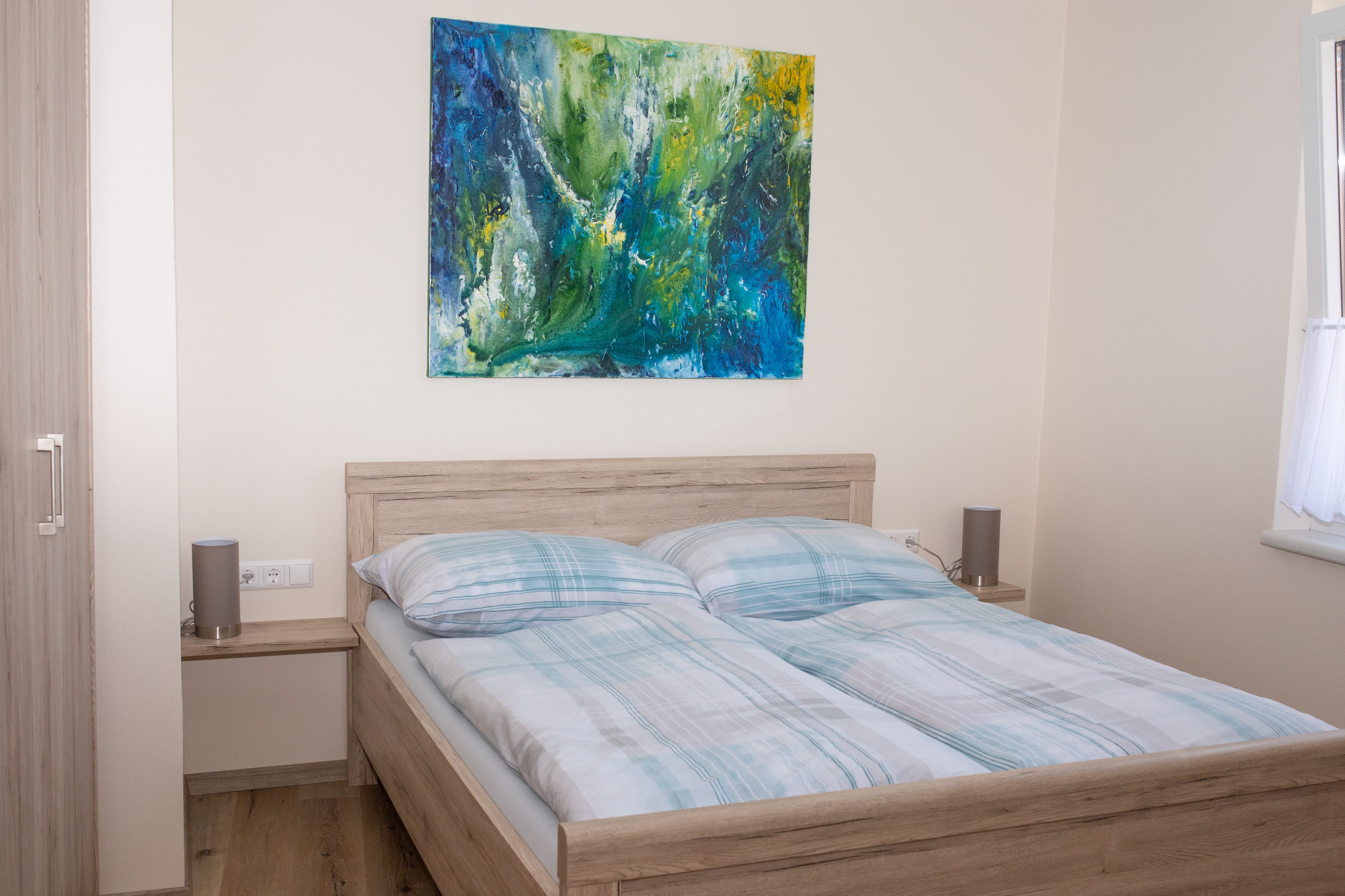 Bedroom with double bed, abstract painting on the wall and window with curtain.