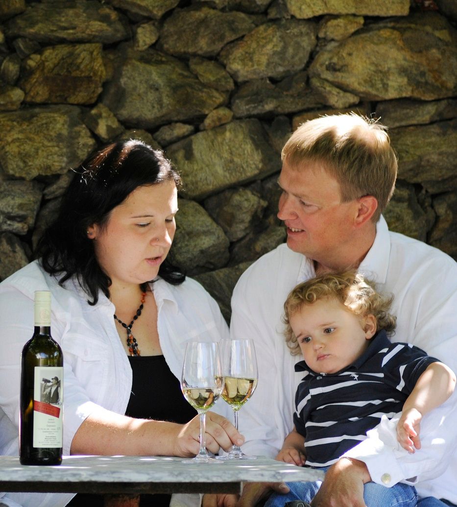 A family sits at a table with two wine glasses and a bottle of wine in front of a stone wall.