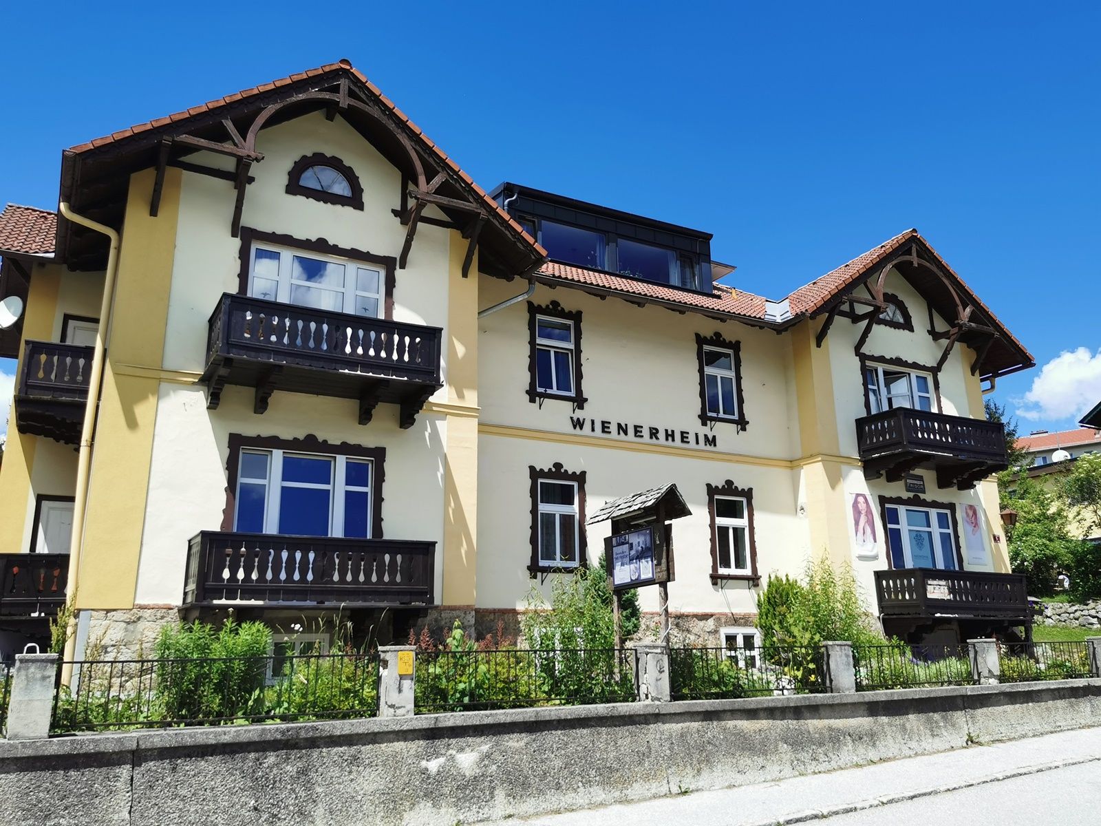 Yellow building with the inscription 'WIENERHEIM', wooden balconies and blue sky.