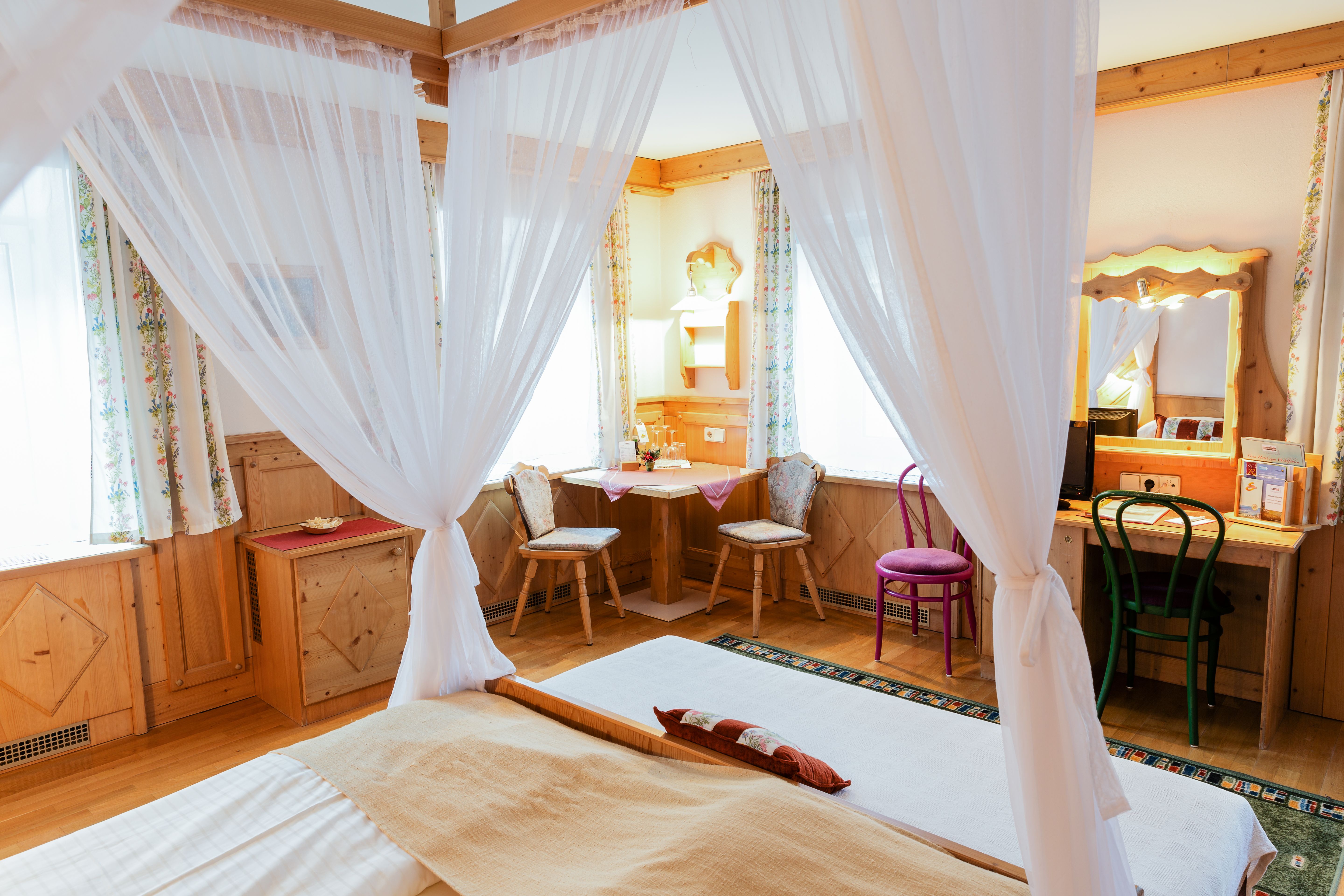 Cozy double room with four-poster bed, wooden furniture and desk.