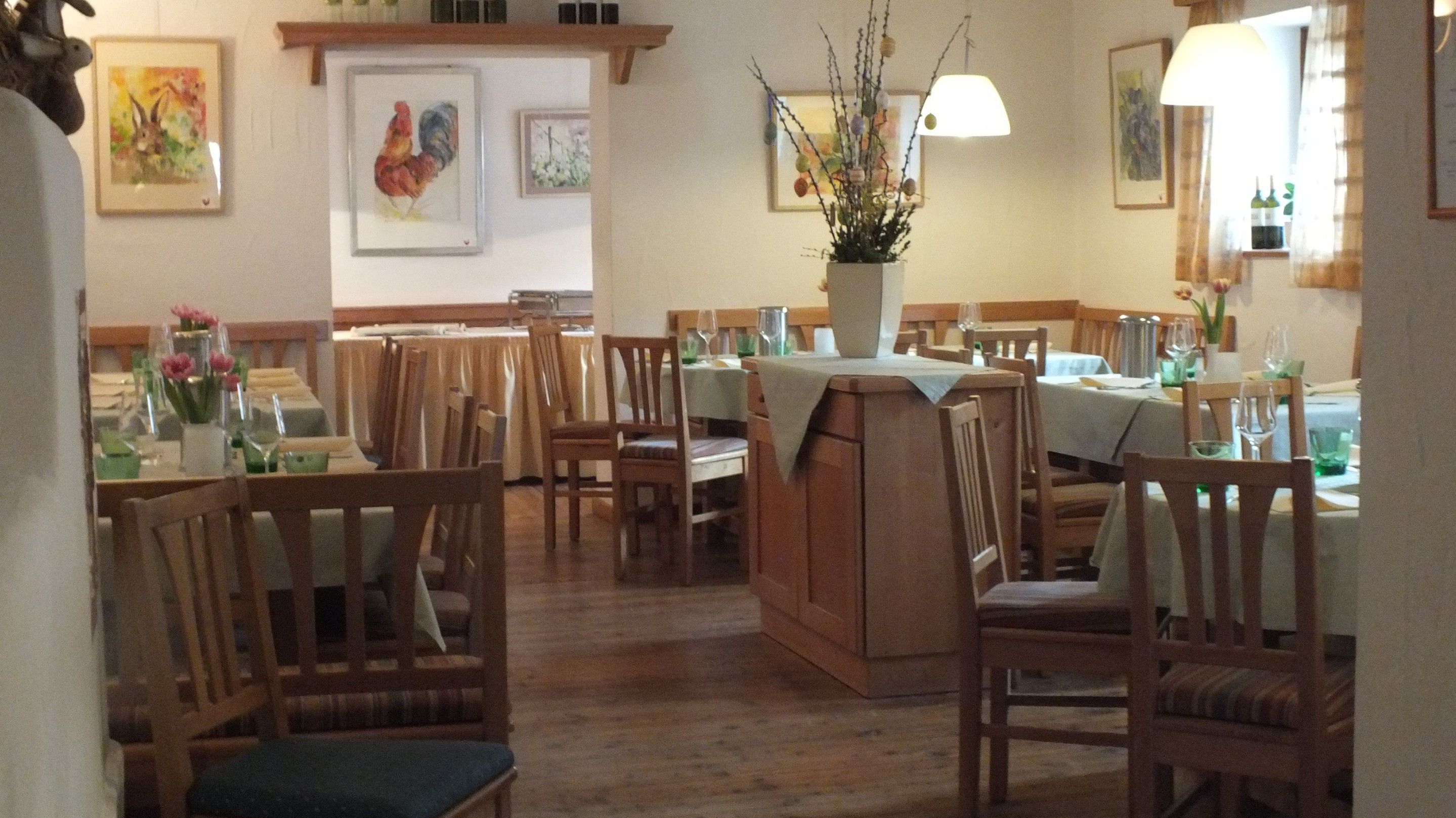 Cozy restaurant with wooden furniture, laid tables and flower vases. Pictures of animals on the walls.