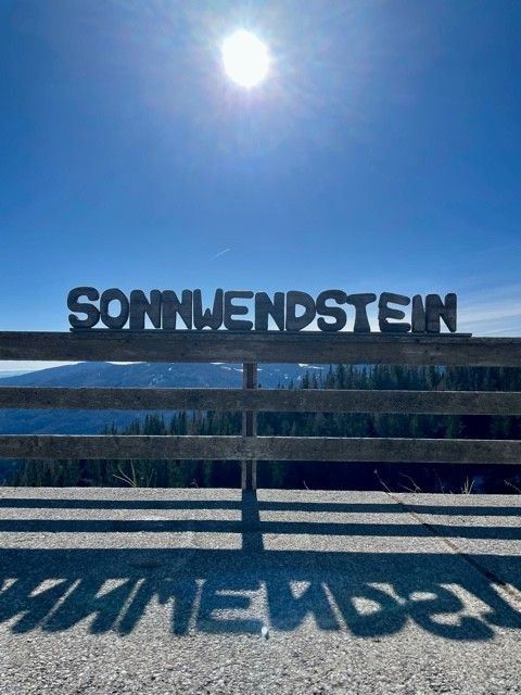 Capital letters with 'Sonnwendstein' in front of a sunny sky and mountain landscape.