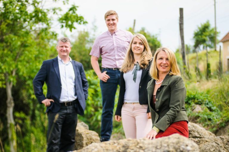 Four people pose outside on a rock, surrounded by trees and plants.