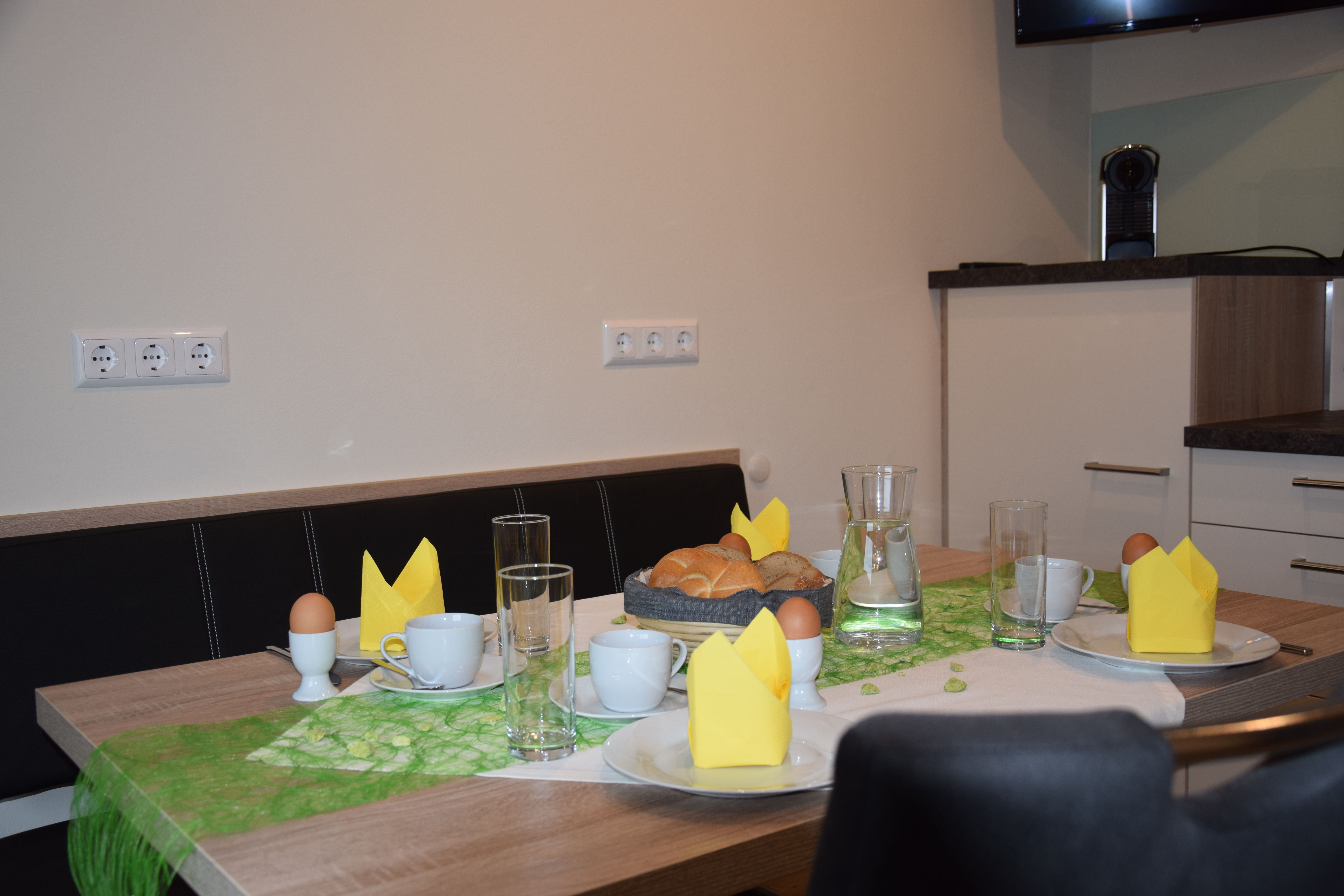 Breakfast table with bread rolls, eggs, cups and yellow napkins.