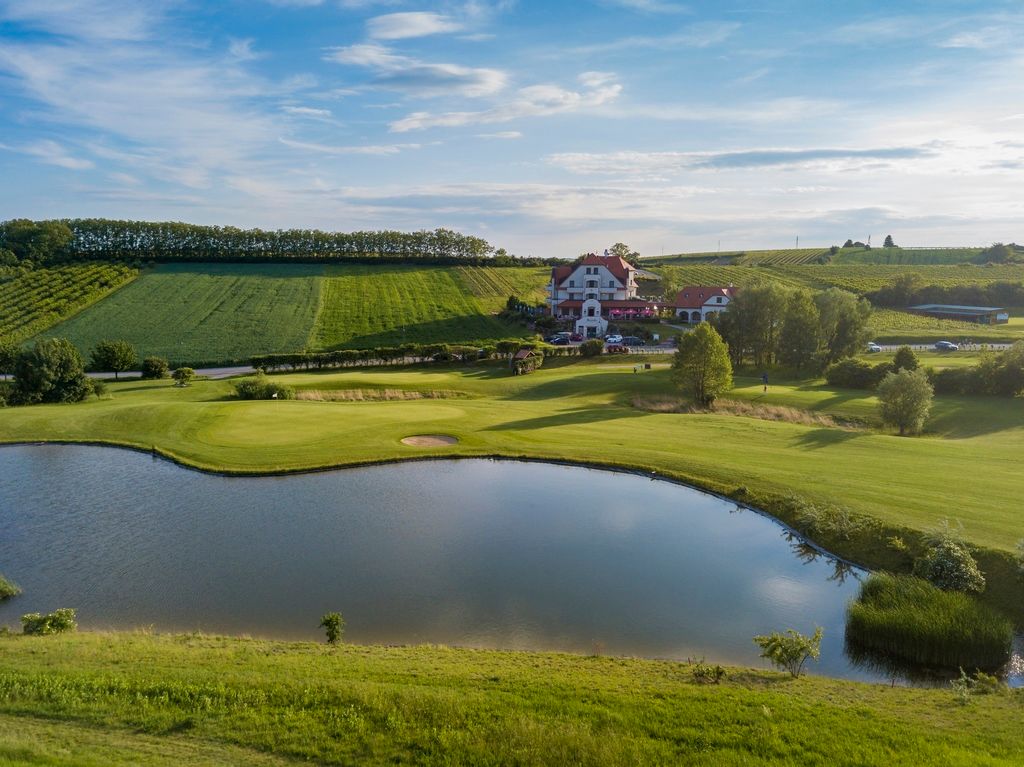 Landscape shot of a golf course with a pond and clubhouse in the background.
