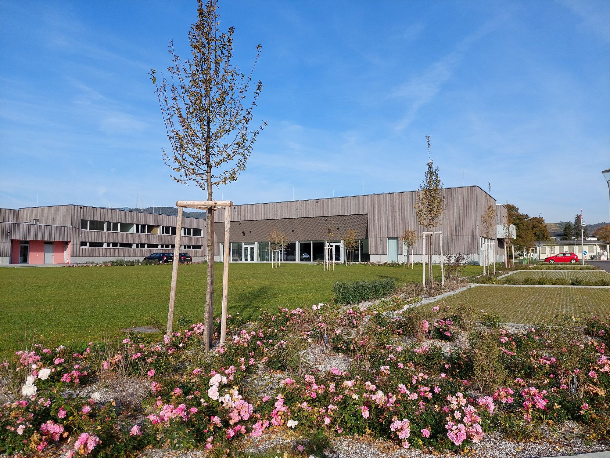 Modern building with wooden façade and well-kept gardens in the foreground.