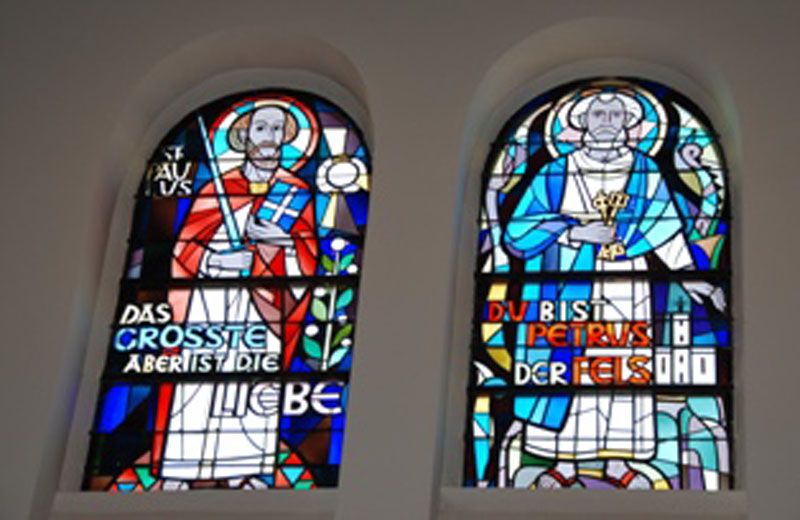Two colorful stained glass windows with religious figures and inscriptions.