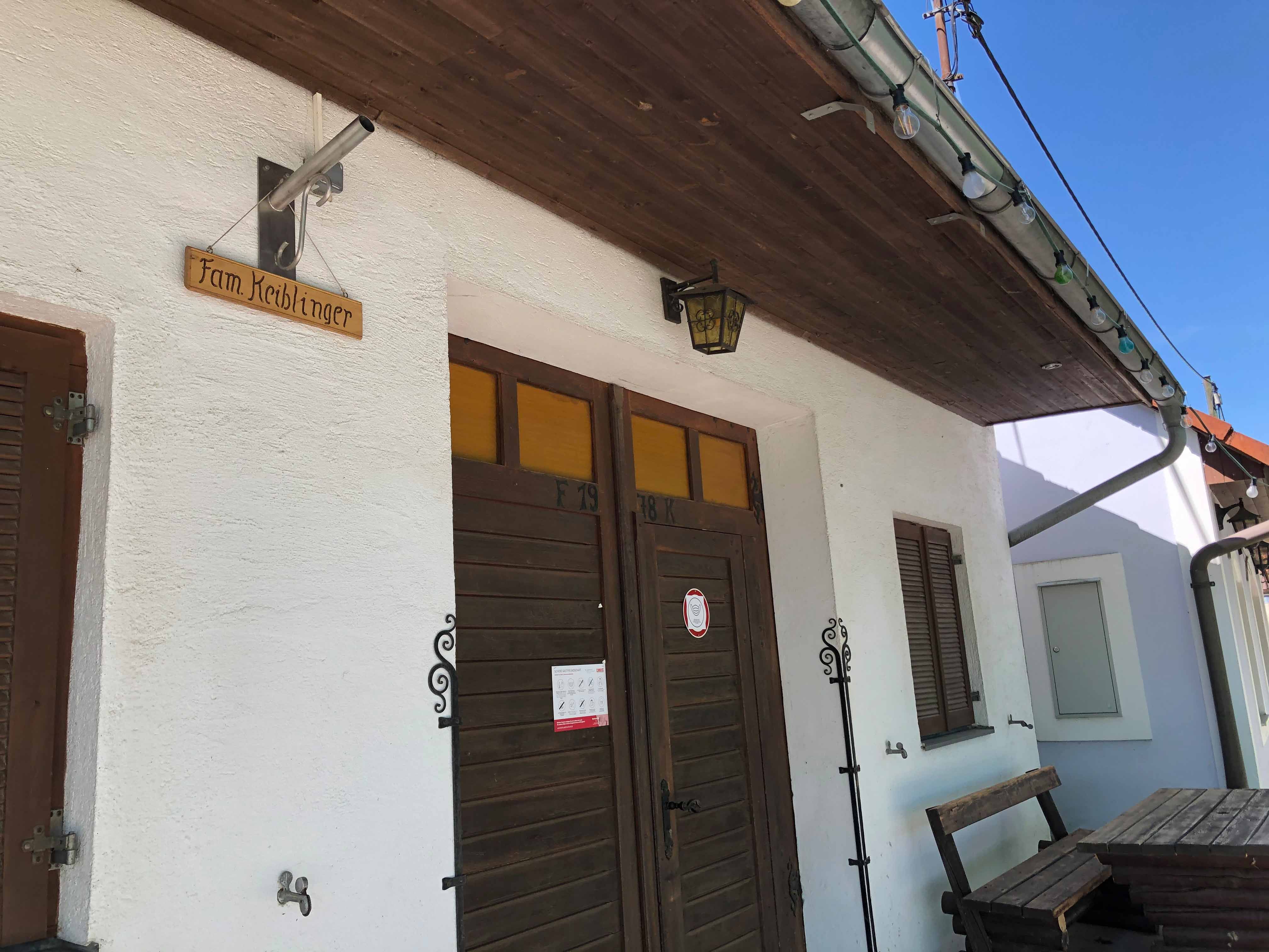 Entrance of a wine tavern with wooden sign 'Fam. Keiblinger'.