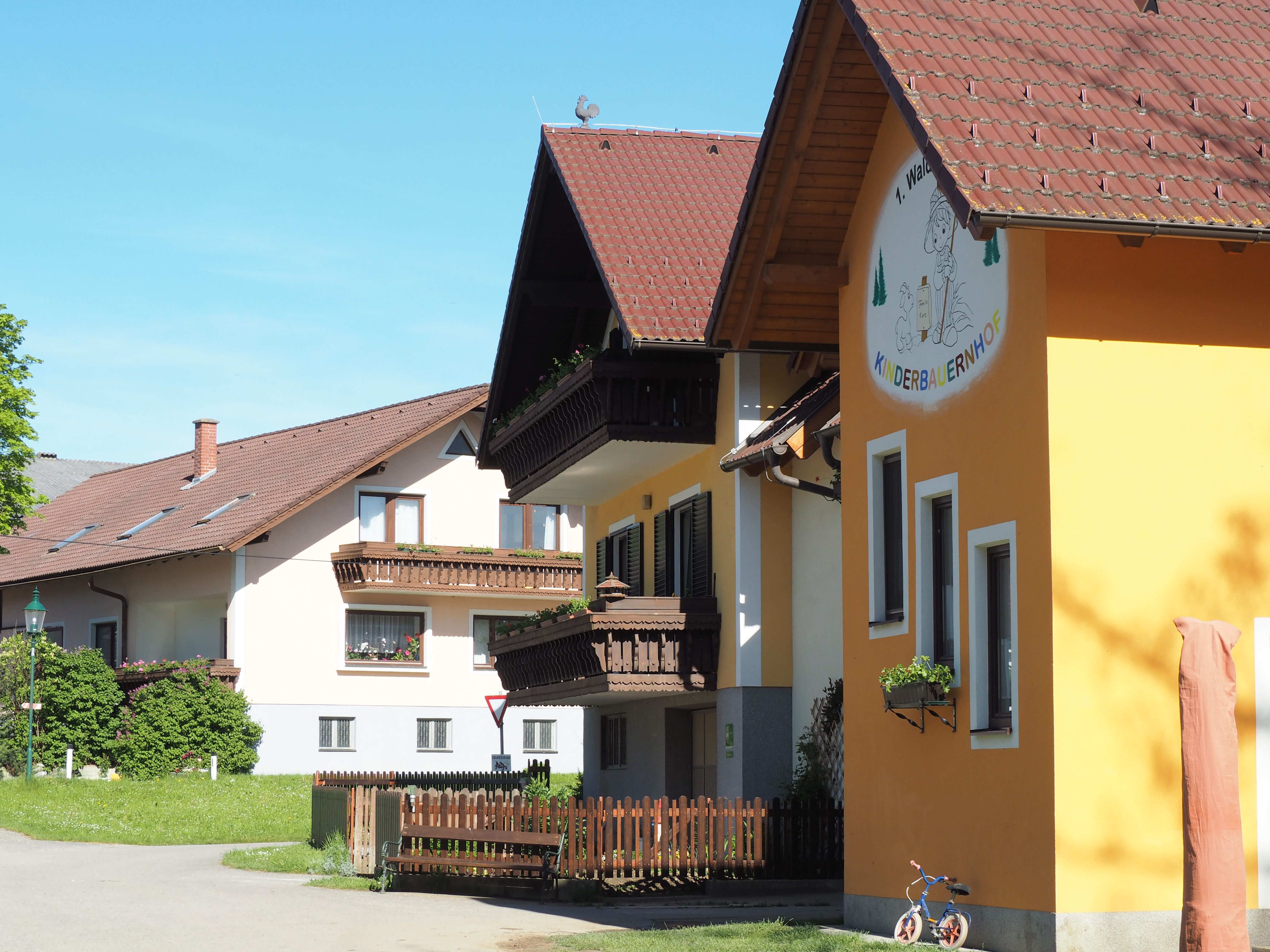 Waldviertel children's farm building with yellow façade and wooden balconies, surrounded by green countryside.