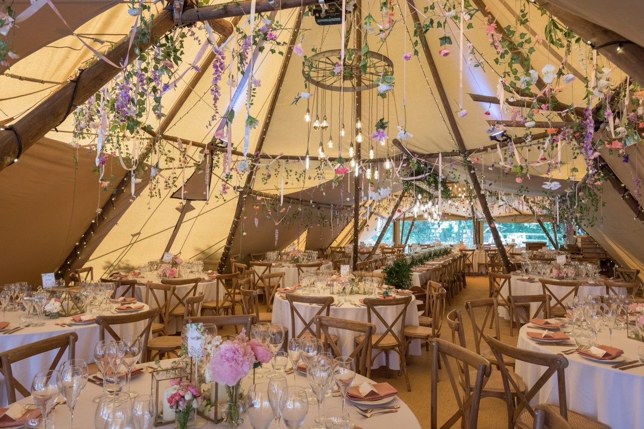 Interior view of a festively decorated tipi with round tables and flowers.