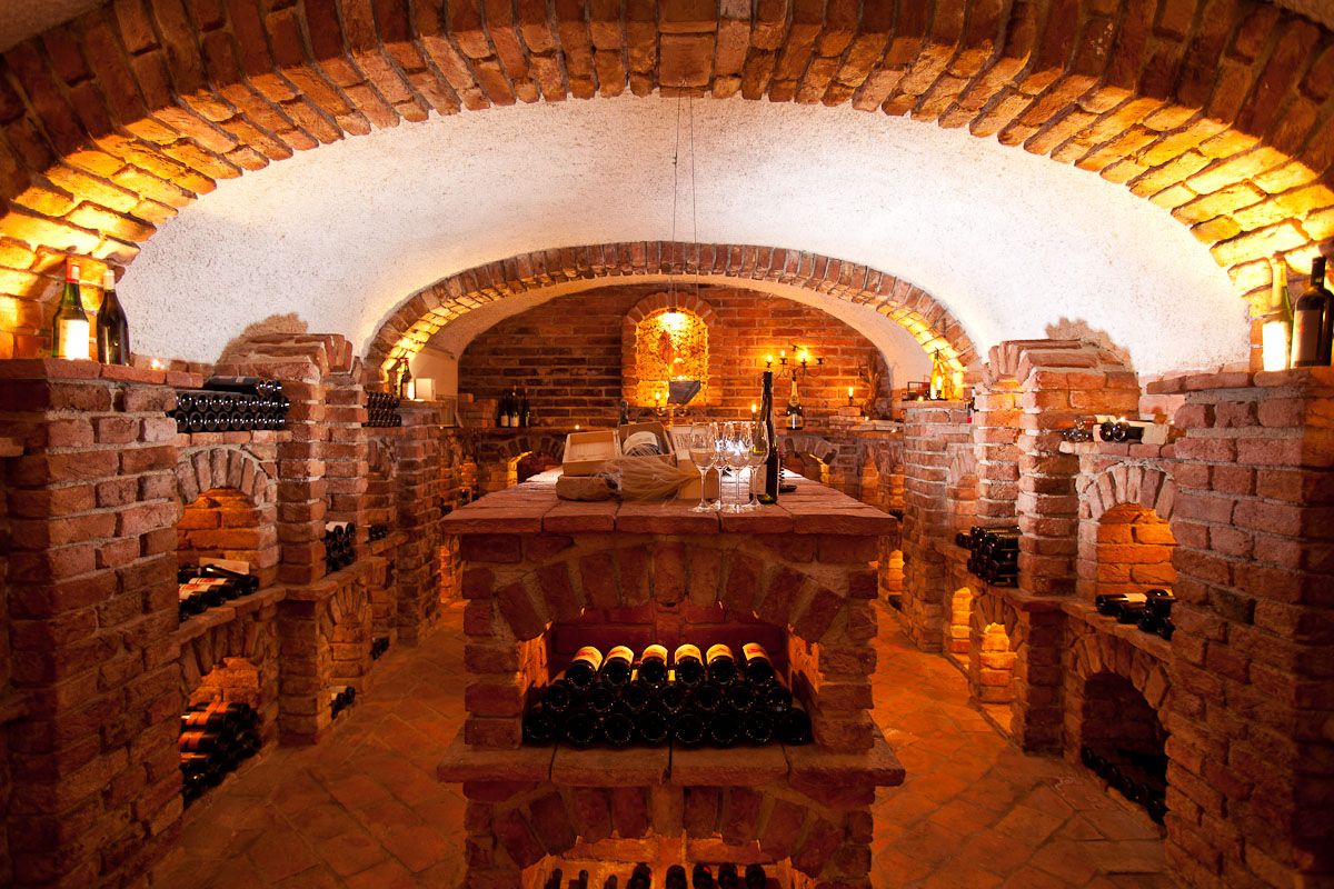 An atmospherically lit wine cellar with brick walls and wine bottles on shelves.