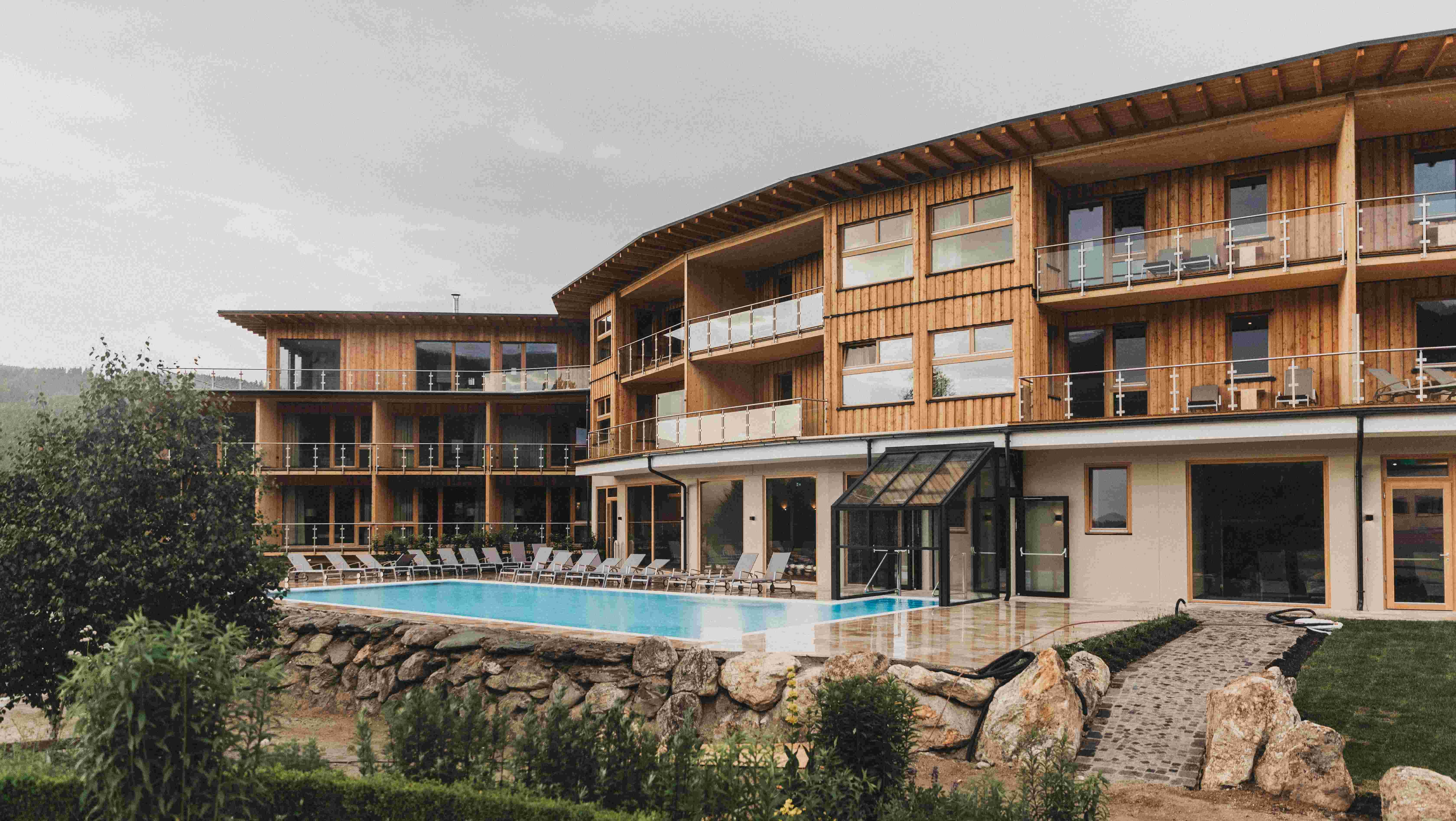 Exterior view of a modern wooden building with pool and sun loungers.