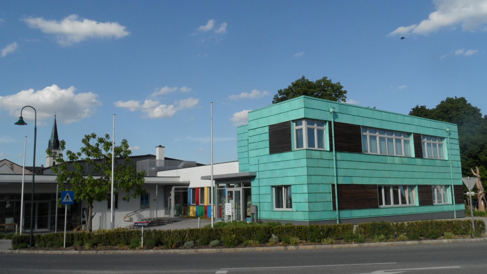 Modern building with turquoise façade in Guntersdorf, with a church tower in the background.