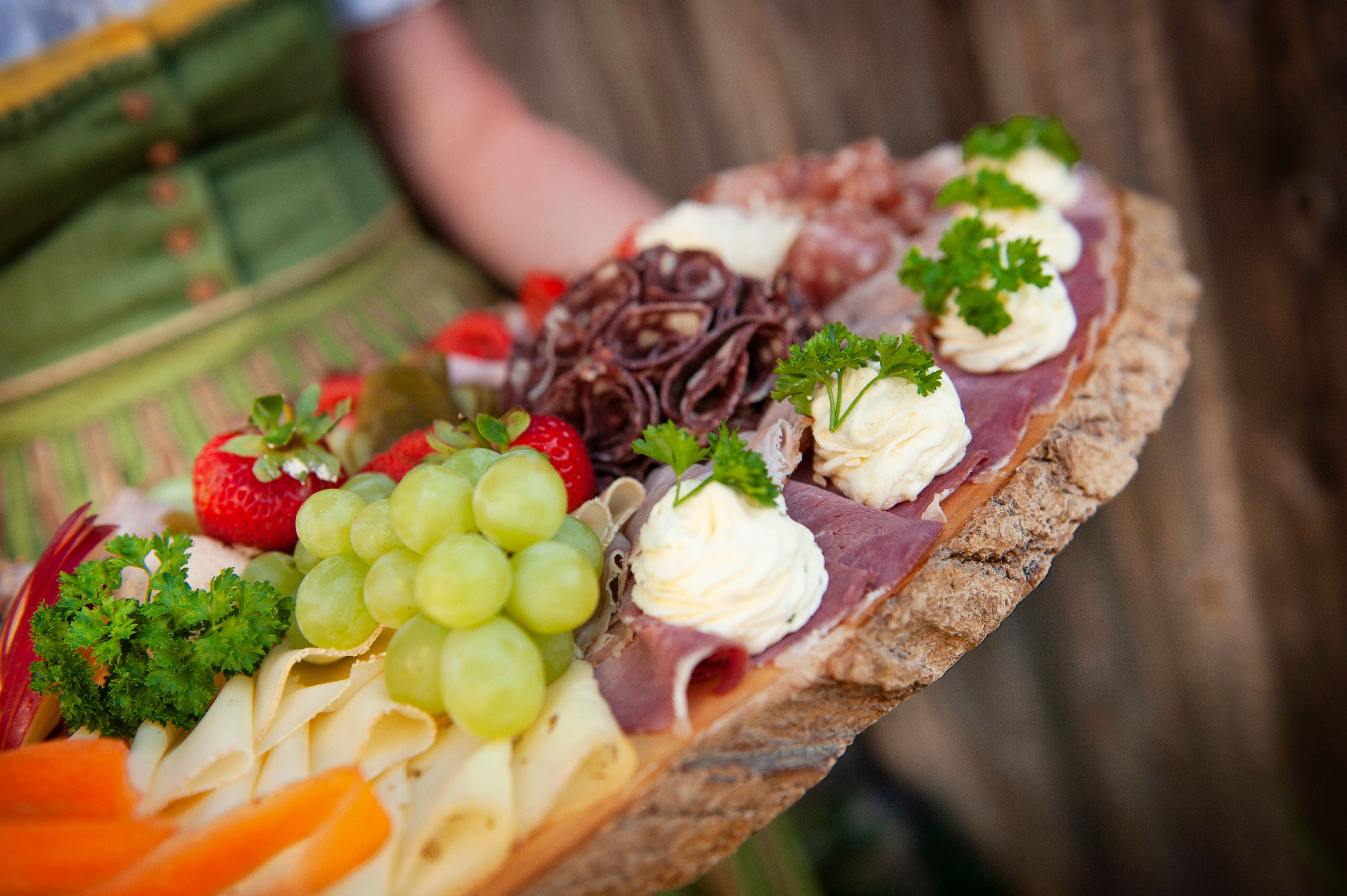 A rustic platter with cheese, ham, grapes, strawberries and herbs.