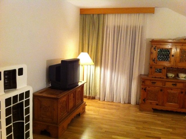 A living room with wooden furniture, an old television, a floor lamp and curtains.