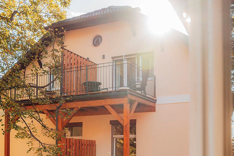 House with balcony and sunshine through trees.