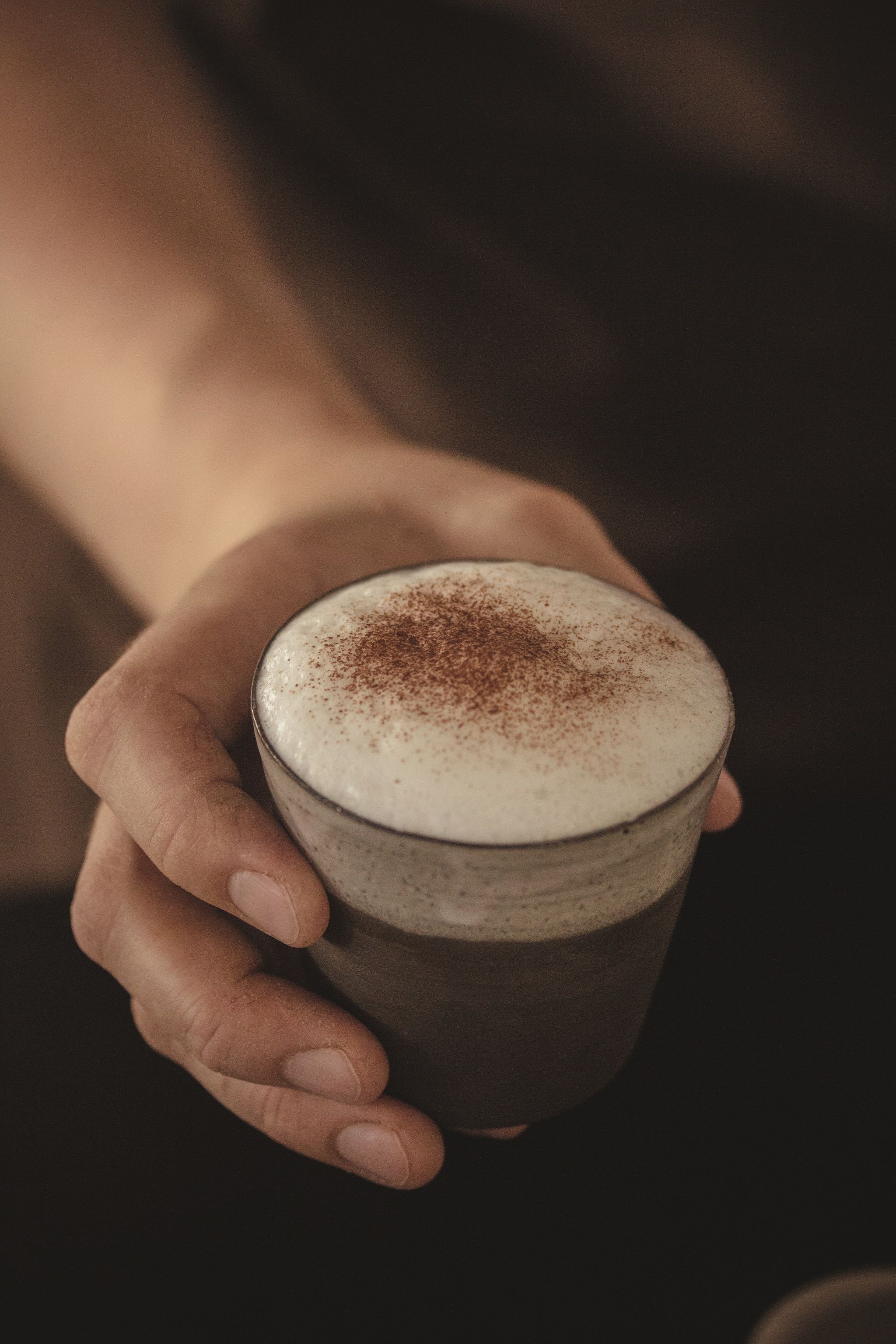 Close-up of a hand holding a glass with cappuccino and milk foam.