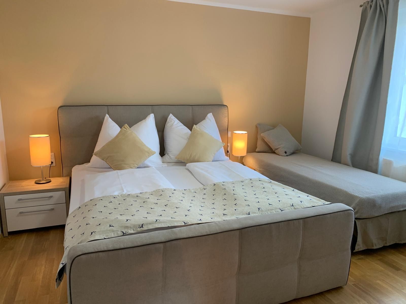 Comfortable bedroom with double bed and single bed, two bedside lamps and curtains.