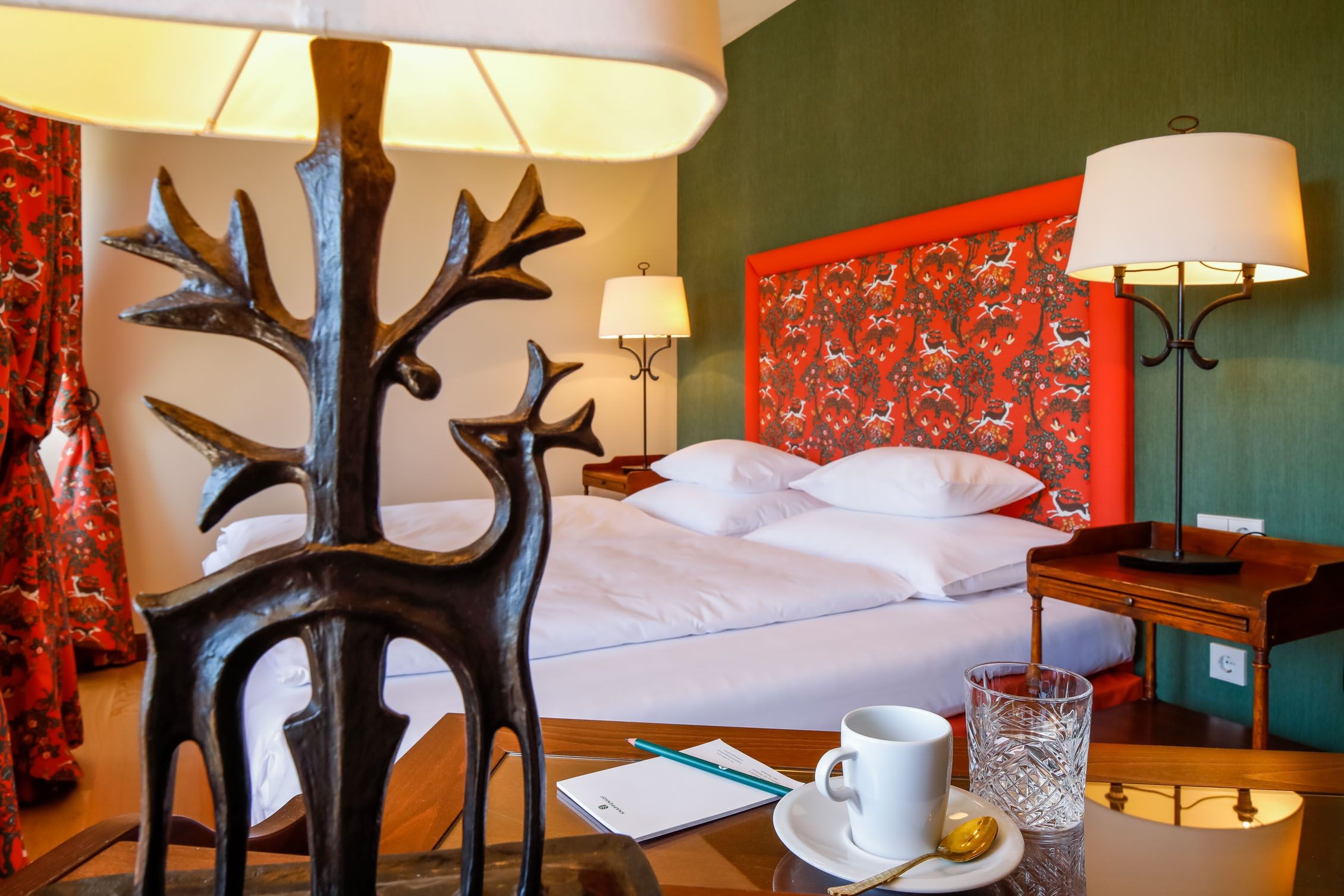 A stylishly furnished hotel room with a bed, decorative lamps and a table with a cup and glass.