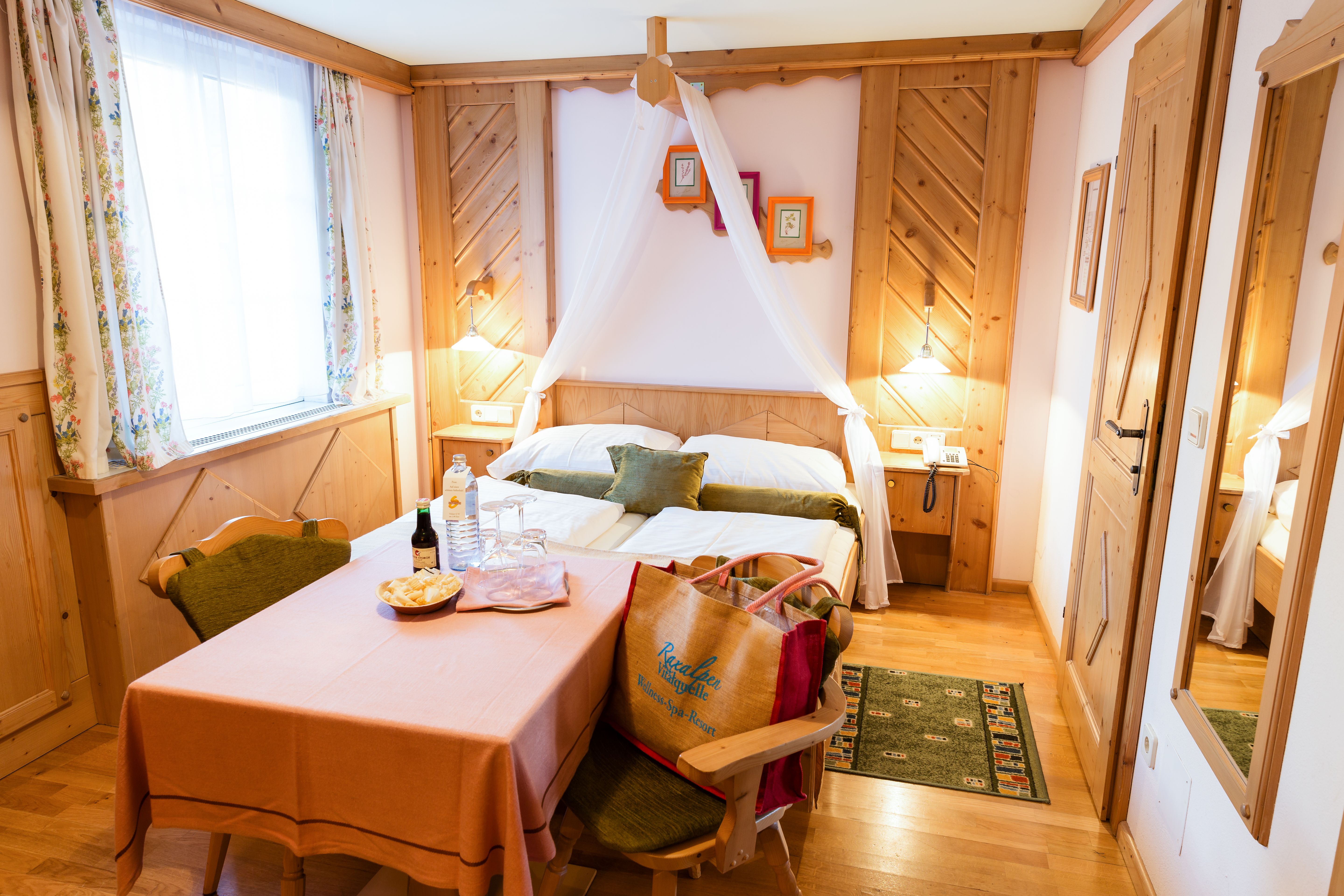 Cozy double room with wooden furniture, a table with drinks and snacks, and a bed with canopy.