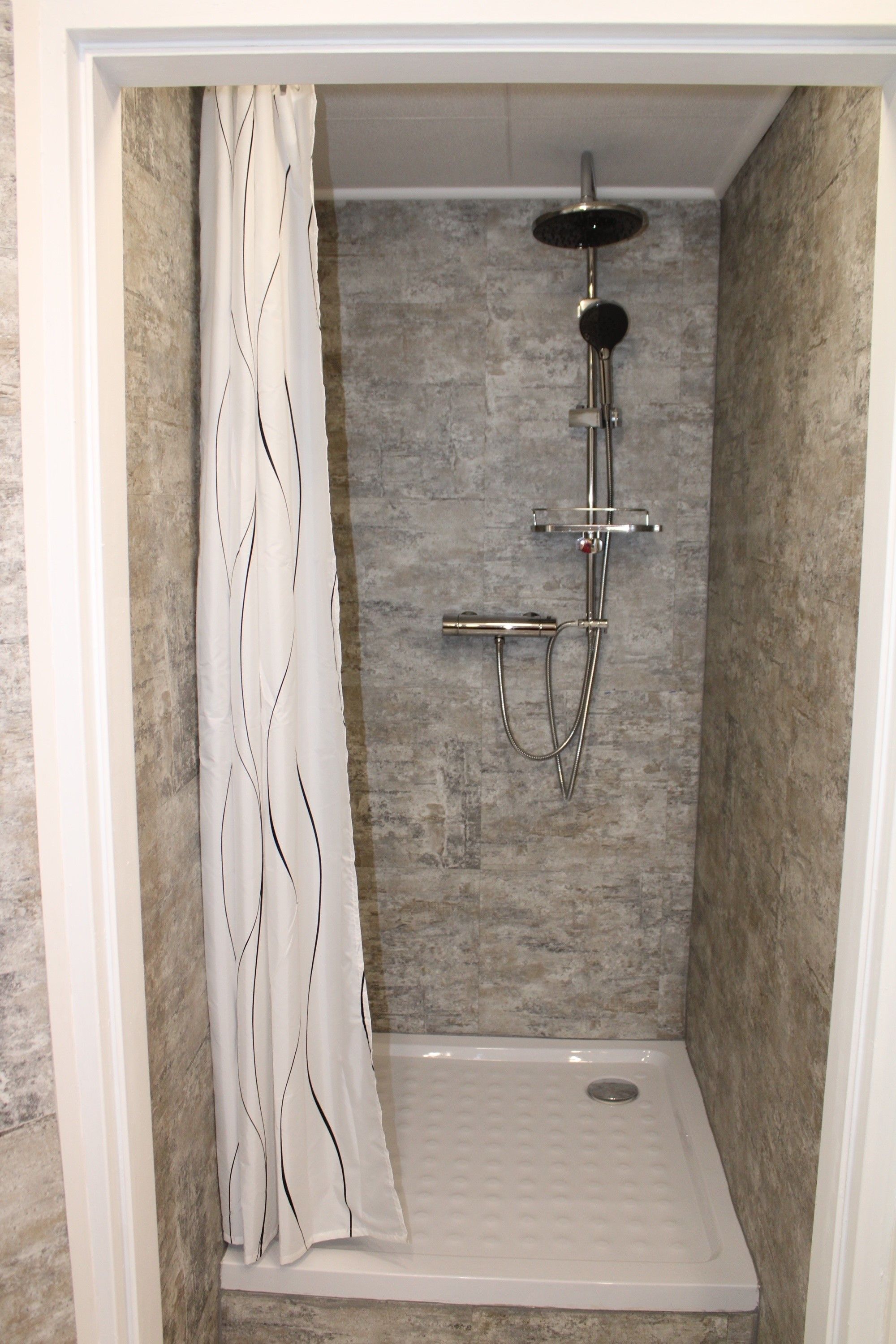 Modern shower with gray tiles and shower curtain.