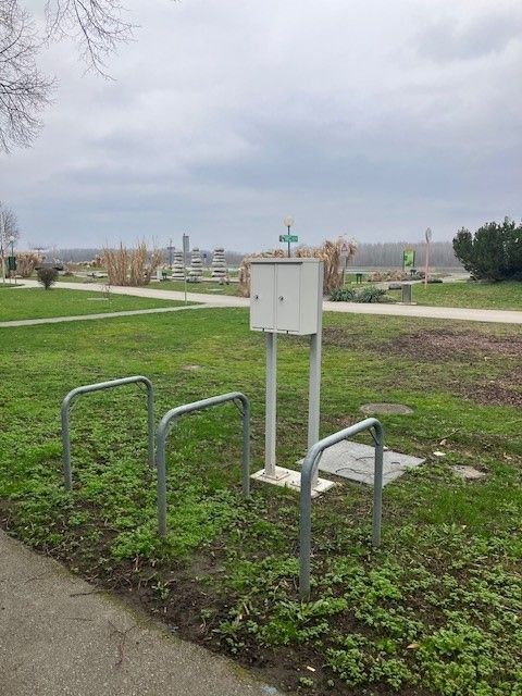 E-bike charging stations on a meadow with bike racks and a path in the background.