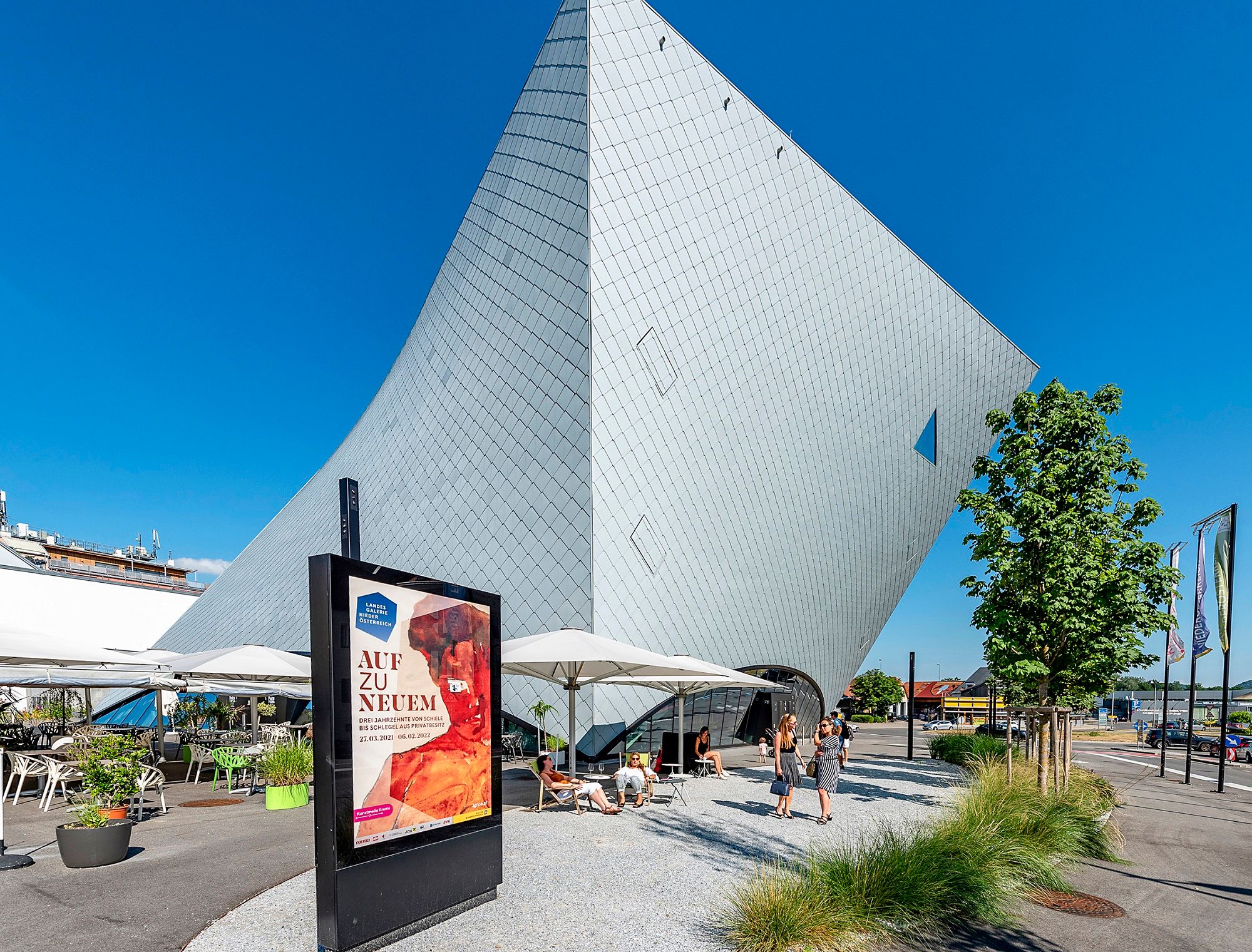 Modern architecture of the Landesgalerie Niederösterreich in Krems with visitors and advertising poster in the foreground.