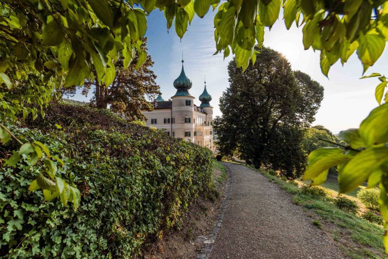 Artstetten Castle with green onion domes, surrounded by trees and a path in the foreground.