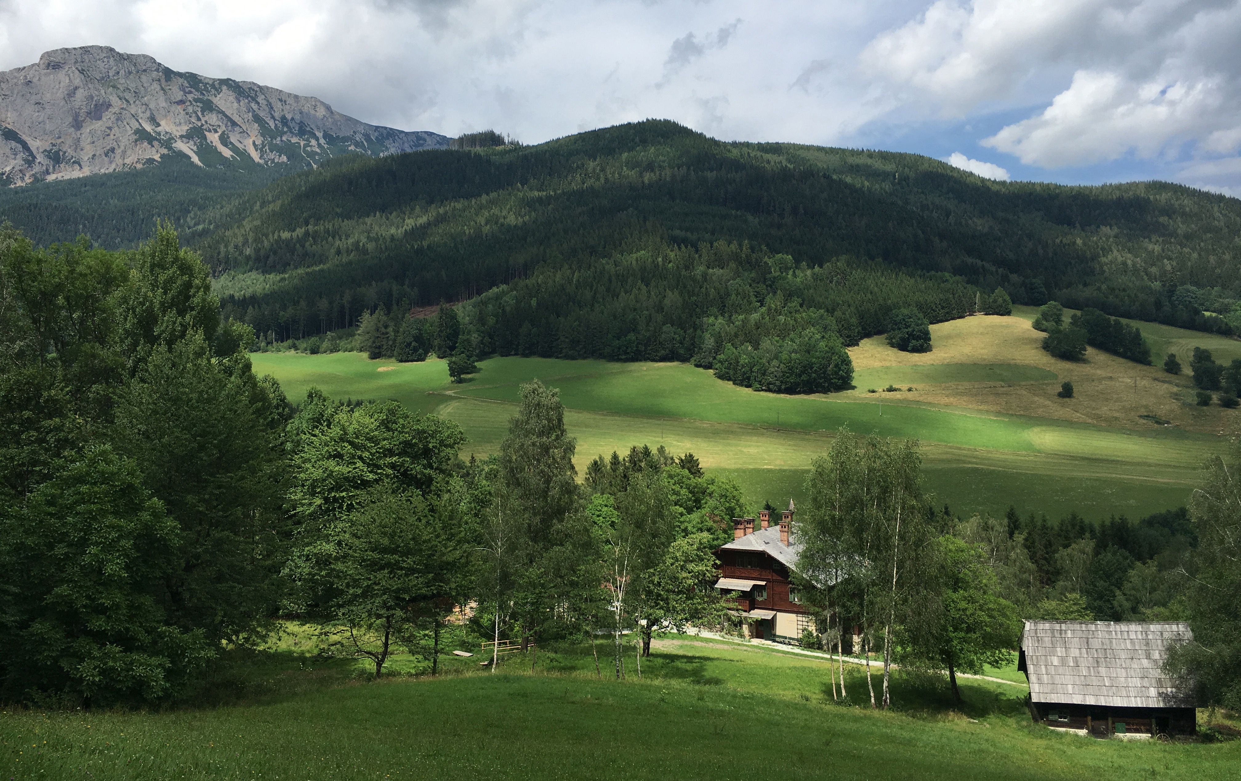 A farm in a green, hilly landscape with mountains in the background.