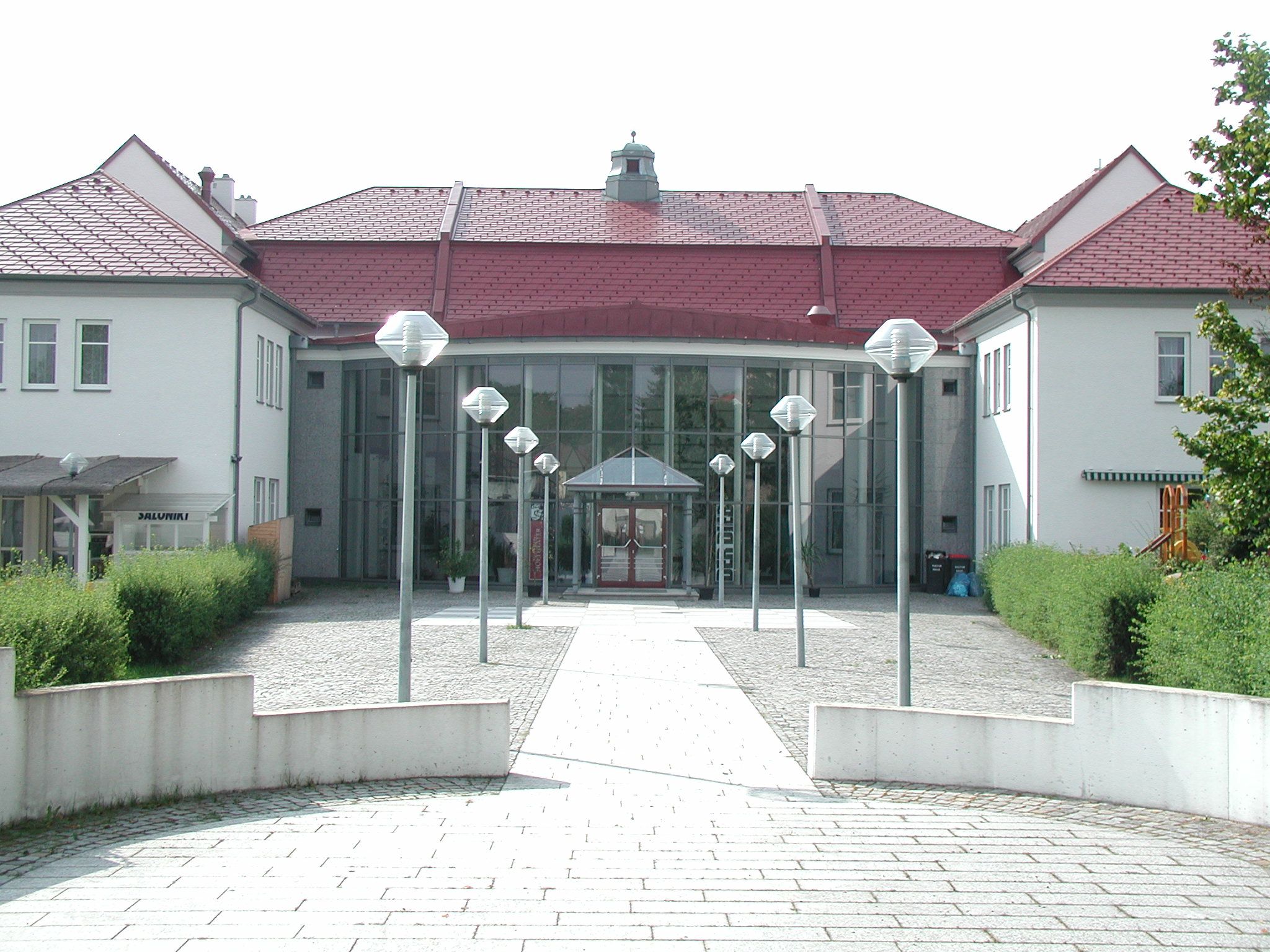 Entrance to a modern cultural center with glass façade and red roofs.