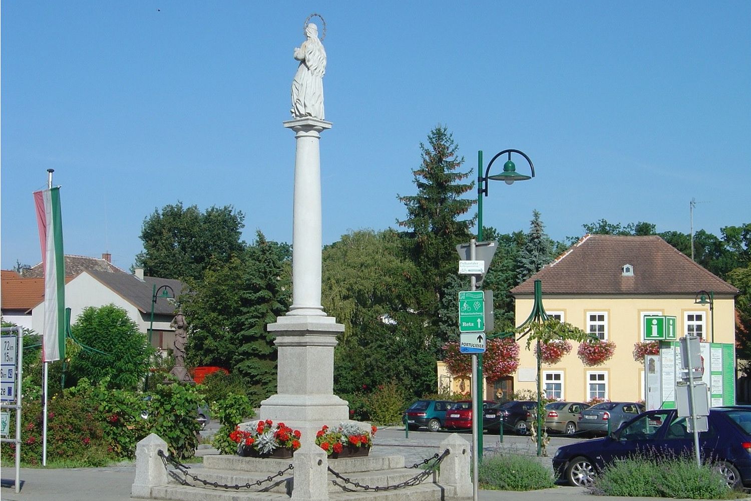 Statue on a column in a square in Haugsdorf, surrounded by buildings and trees.